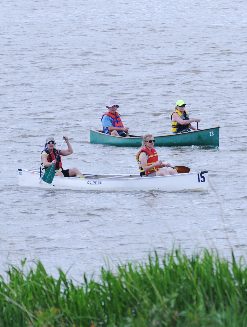 Two canoes with paddlers wearing life jackets navigating a calm river.